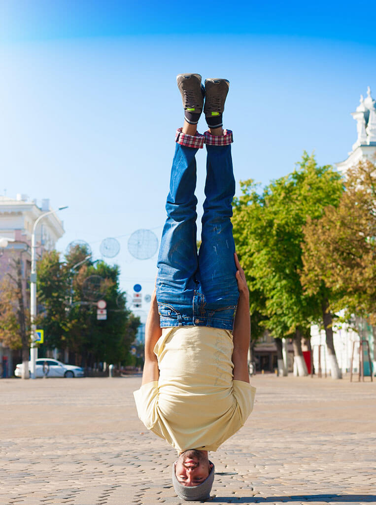 Man, preforming handsfree headstand on an urban cityscape just like us ensuring that no detail is missed on your Creative quest  
